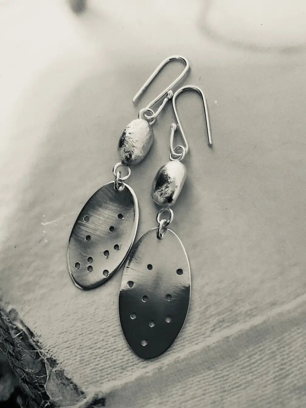 Brass oval drop earrings with perforated dot pattern and silver nugget accent, black and white filter